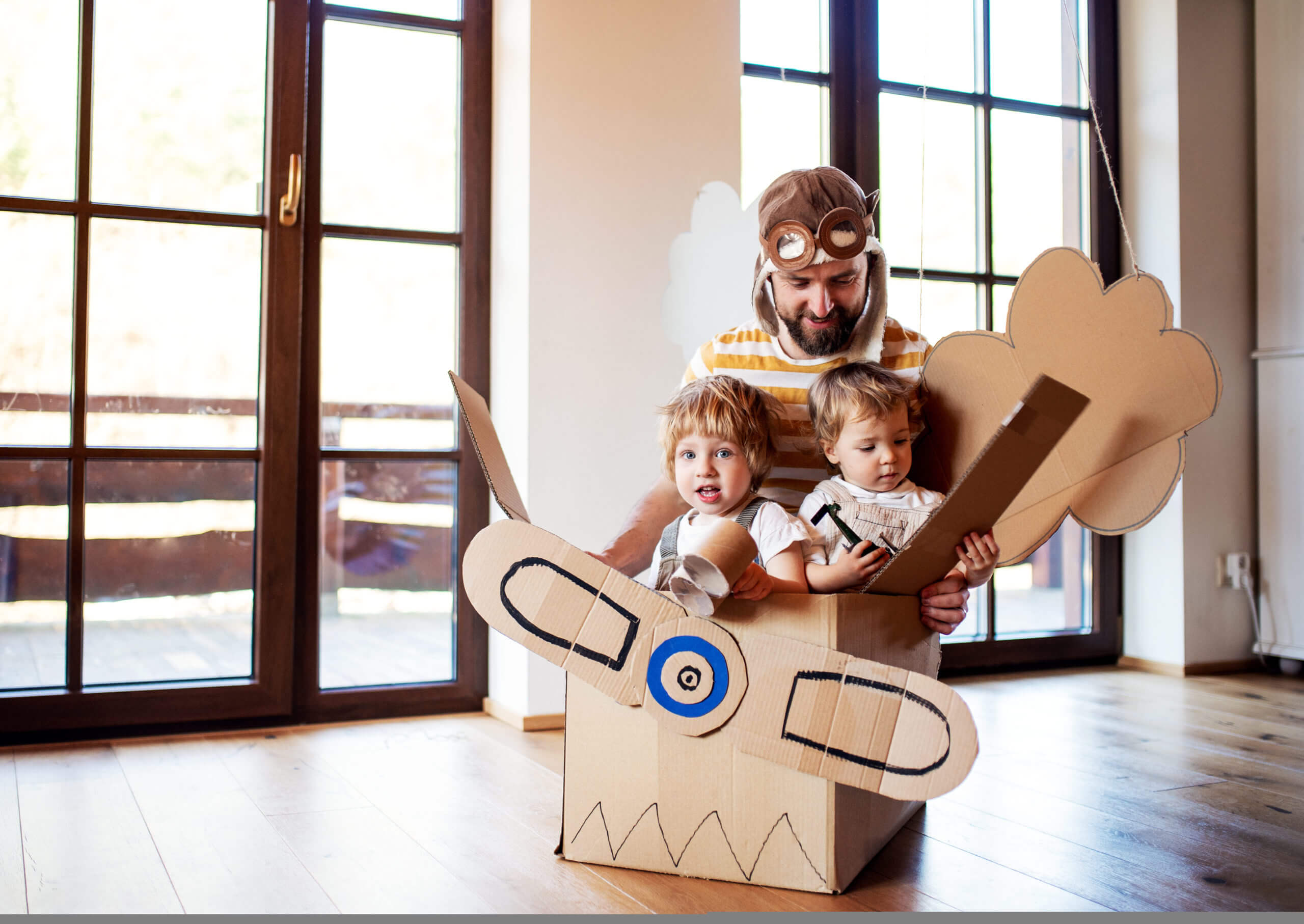 A father and toddler chidlren playing with carton plane indoors at home.